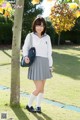 A woman in a school uniform standing next to a tree.