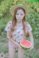 A woman in a straw hat holding a watermelon.